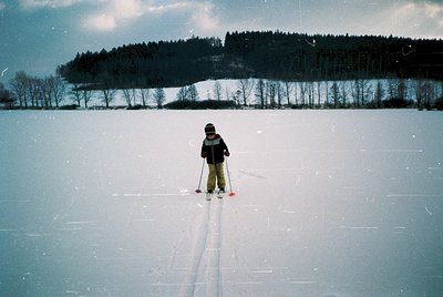 Child cross-country skiing on groomed trail, surrounded by snow-covered landscape. Barren trees and distant forested ridge un...