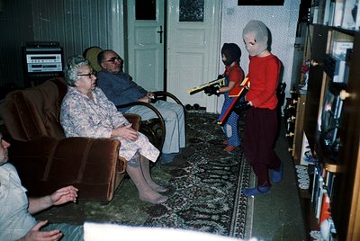 Vintage living room scene from the 1970s featuring a family in casual attire. Elderly couple seated on a floral-patterned sof...