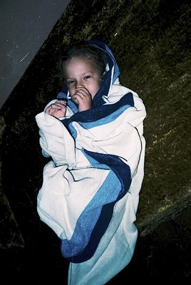 Young child wrapped in a vintage-style blanket with blue and white stripes, posing indoors near a dark, reflective surface. T...