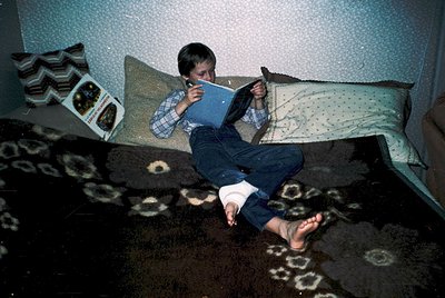 Vintage 1970s-style living room scene: boy engrossed in a book on a patterned sofa, barefoot with rolled-up jeans. Decor incl...