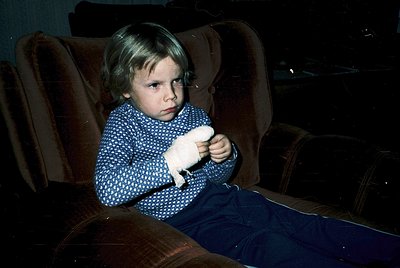 Young child in mid-20th century cinema setting, clutching a white stuffed animal. Dark theater seats and dim lighting evoke 1...