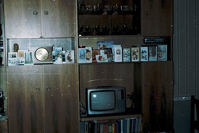Mid-century wooden cabinet showcasing vintage Soviet-era decor: framed holiday/postcards, a round wall clock, and a CRT TV at...