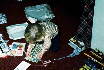 Child arranging wrapped gifts on a carpeted floor, surrounded by various packages and a plaid blanket. Notebook with Cyrillic...