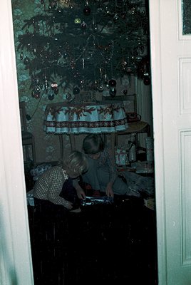 Reflection of two children playing with a board game in a dimly lit, vintage interior. Decor includes ornate glass ornaments,...