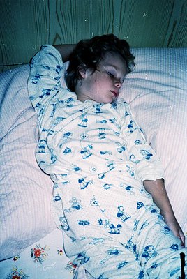 Child sleeping in vintage floral-patterned pajamas with blue nautical motifs, lying on a hospital-style bed with a neutral bl...