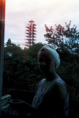 Vintage photo of a woman in a headscarf seated indoors, framed by a window overlooking a lush, forested area. A distinctive r...