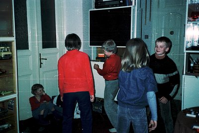 Vintage indoor scene featuring five children (ages ~8-12) in a dimly lit room with white-painted walls and built-in shelving....