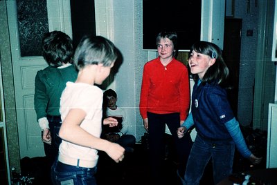 Vintage indoor scene of four teens playing a game, likely in the 1980s. Bright colors—red sweater, blue jacket, green shirt—h...