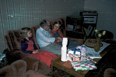 Vintage indoor scene featuring three generations: an elderly couple and a young girl in a living room, likely . The woman hol...