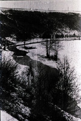 Aerial view of a winding river bordered by leafless trees, likely winter or early spring. Snow patches and barren landscape s...
