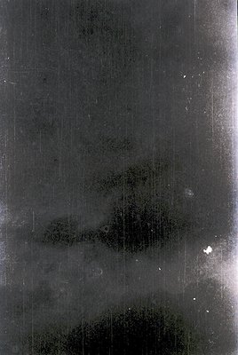 Vintage black-and-white photograph of a blurred, abstract urban scene—likely a street or courtyard with indistinct vertical l...