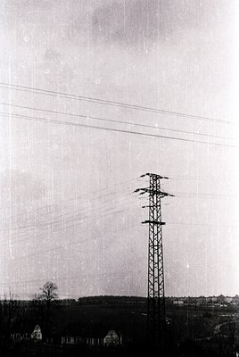 Mid-century industrial landscape featuring a tall lattice steel transmission tower with high-voltage lines stretching horizon...