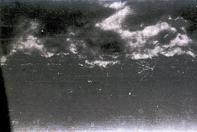 Vintage aerial photograph showing low-contrast cloud formations over a flat, possibly agricultural or urban landscape. Textur...