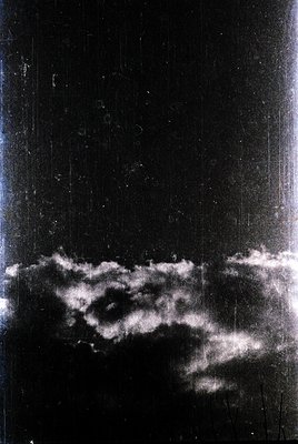 Vintage sepia-toned photograph of low-hanging clouds over a dark, possibly industrial or urban horizon. The sky dominates 70%...