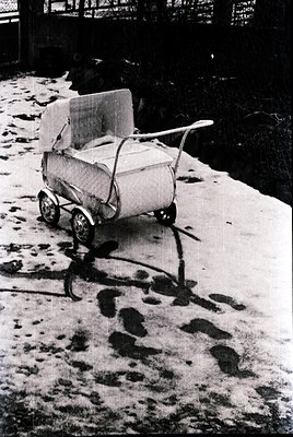 Vintage wooden baby buggy with canvas cover on snow-covered path, mid-20th century. Distinctive curved handle and four wheels...