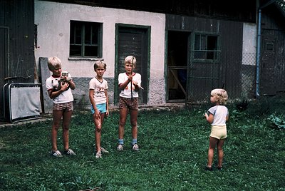 Four children pose outdoors in 1970s-era clothing—short-sleeve shirts, knee-length shorts, and sneakers—holding toy guns in a...