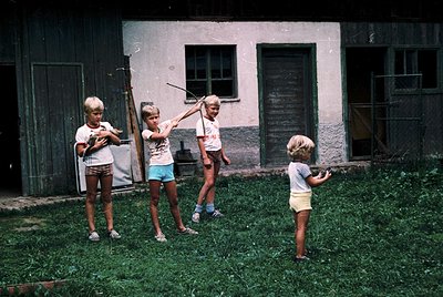 Four children play frisbee in a grassy courtyard beside a weathered concrete building, likely a 1970s Eastern Bloc residentia...