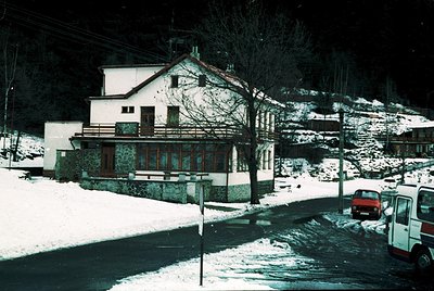 Two-story alpine chalet-style building with stone foundation and wooden accents, set against snow-covered slopes. Snow-laden ...