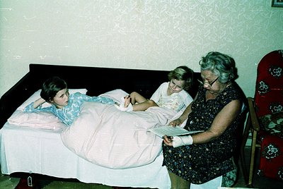 Vintage hospital room interior featuring two women and a young girl on a twin bed. The older woman, dressed in a floral blous...