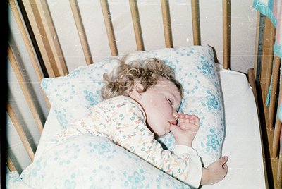 Vintage-style close-up of a child peacefully sleeping in a crib with floral-patterned blanket, likely mid-20th century. Soft ...