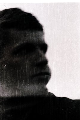 Silhouette portrait of a man with short hair and a mustache, captured in high-contrast monochrome. Raindrops streak the frame...