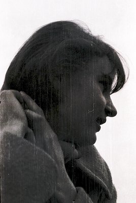 Portrait of a person standing under a rain shower, water droplets visible on face and clothing. The scene captures a candid, ...