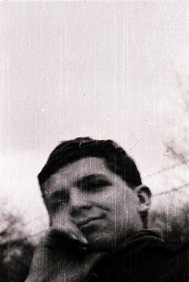 Black-and-white portrait of a young man in a military-style cap, captured mid-smoke. Uniform suggests mid-20th century, likel...