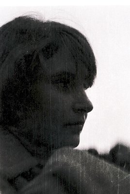 Black-and-white portrait of a person with short, wavy hair and a side profile view, captured through a slightly blurred, text...