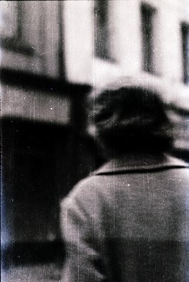 Blurred mid-century street scene featuring a person in profile, likely mid-20th century. Lighting suggests indoor-outdoor tra...