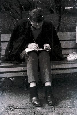 Mid-20th century man writing in an open notebook on a wooden bench, dressed in a suit and tie with knee-high socks and loafer...