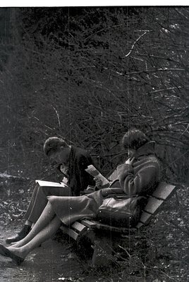 Sculpture of two seated figures reading on a stone bench, set against a rocky, tree-lined background. Likely mid-20th century...