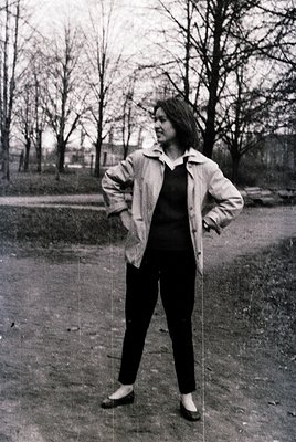 Portrait of a person in a 1960s-70s urban park, wearing a structured blazer, turtleneck, and tailored trousers. Leaves sugges...
