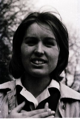 Portrait of a young woman with short, layered hair, smiling naturally. She wears a collared jacket with a subtle pattern, lik...