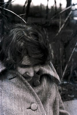 Vintage black-and-white portrait of a young woman in mid-laugh, her hair windswept. She wears a buttoned coat with a visible ...