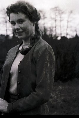 Black-and-white portrait of a woman in mid-20th-century fashion—side profile, hair styled in a side-swept bob, wearing a coll...