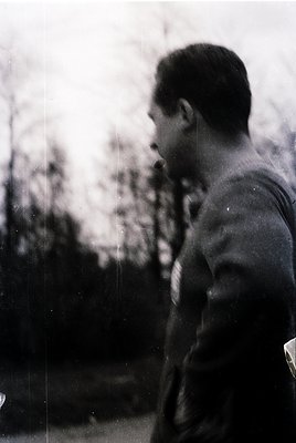 Portrait of a man in a sleeveless shirt, holding a cigarette, outdoors with blurred greenery in background. Vintage monochrom...