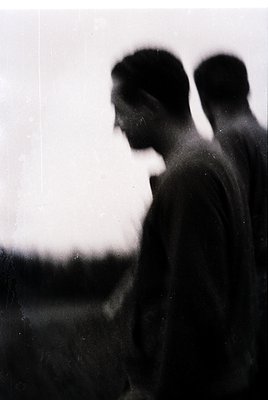 Silhouetted figures in mid-20th-century attire, blurred by vintage film grain, stand against a hazy horizon. Likely a coastal...