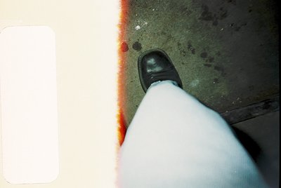 Vintage close-up of a man’s formal shoe (black oxford) and sock crossing a faded red/white painted line on concrete. Likely m...