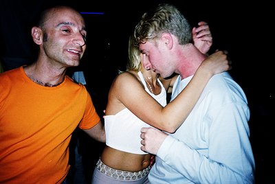 Intimate moment captured at night: two men embracing with playful affection, one in an orange shirt, the other in a light blu...