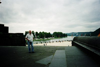 A man in a light-colored shirt and jeans poses on a concrete ledge overlooking a flooded urban waterfront. Concrete barriers ...