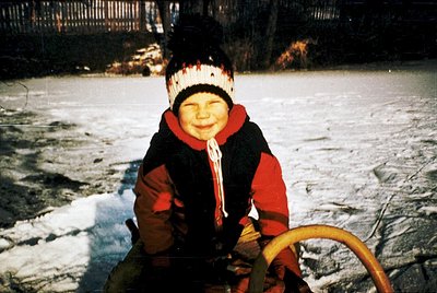 Vintage winter scene of child in winter gear—red scarf, knit hat, and brown/red jacket—sitting on a wooden sled on icy terrai...