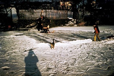 Vintage winter street scene with two children sledding on a snow-covered road. One child in a red jacket and cap rides a sled...