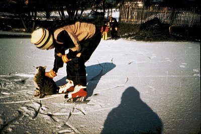 Vintage winter scene: man in 1970s attire (hat, jacket, trousers) kneeling to pet a cat on a sled with red handle. Snow-cover...