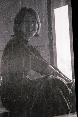 Portrait of a woman seated indoors, holding a book or notebook. Short, layered hair and a high-neck sweater suggest mid-20th ...