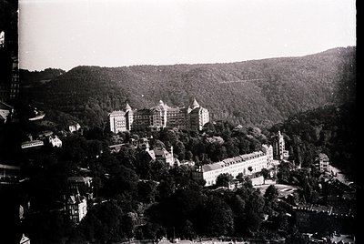 Aerial view of a grand hillside resort complex, likely from the early-to-mid 20th century. Prominent multi-story buildings wi...