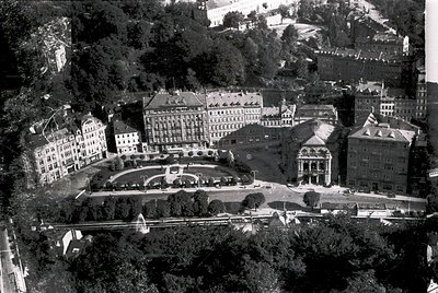 Aerial view of a grand, symmetrical European resort complex from the mid-20th century. Central building features classical ar...