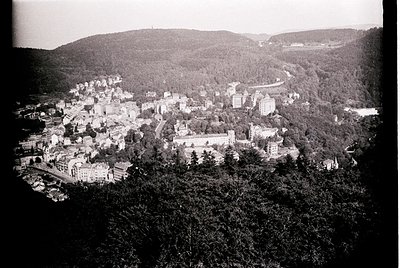 Aerial vintage photograph of a hillside town nestled between forested slopes, likely early 20th century. Prominent castle-lik...