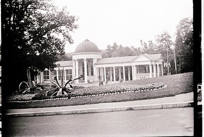 Neoclassical pavilion with domed rotunda and colonnade, set in a landscaped garden with symmetrical flower beds and palm-like...