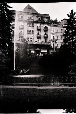 Historic European hotel with Art Nouveau façade, featuring ornate balconies and a central gable. Prominent fountain in foregr...