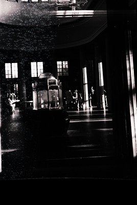 Vintage black-and-white interior shot of a grand, dimly lit ballroom with ornate chandeliers and mirrored walls. Symmetrical ...